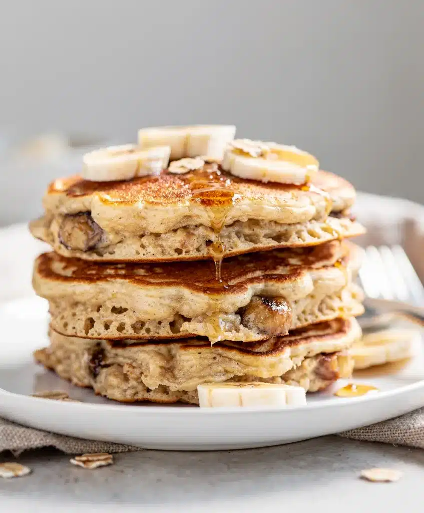 Fluffy banana oatmeal pancakes with maple syrup and walnuts on rustic table