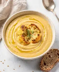 Creamy roasted garlic cauliflower soup in a rustic bowl with thyme.