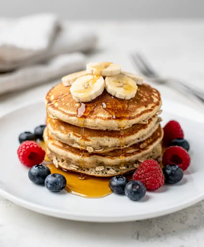 Banana oat pancakes with maple syrup and blueberries on a white plate