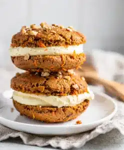 Moist carrot cake whoopie pies with creamy frosting filling on rustic board.