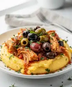 Crockpot tomato olive chicken with savory sauce over creamy polenta or pasta.