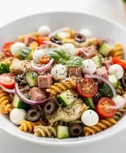 Colorful Italian pasta salad with salami, mozzarella, and fresh vegetables in a bowl.