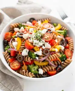 Colorful whole wheat veggie pasta salad with creamy feta and glossy vinaigrette dressing.