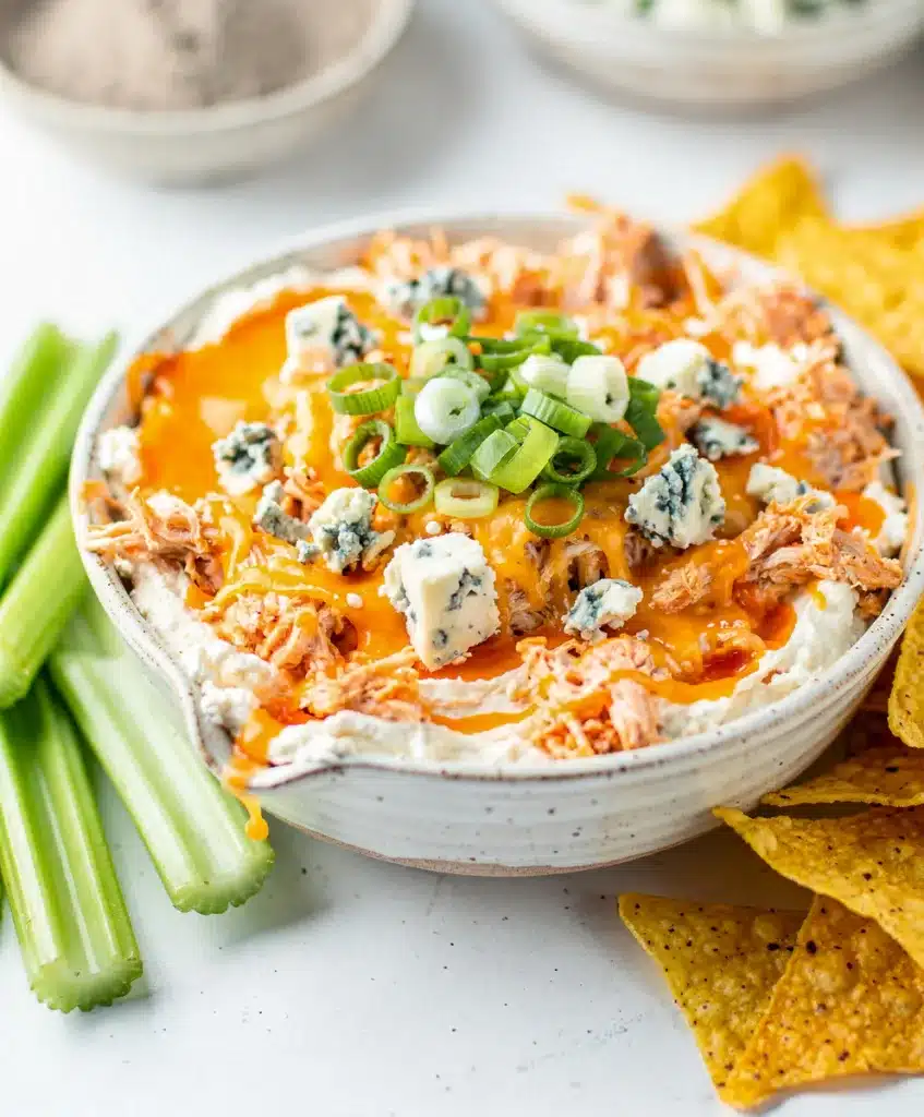 Buffalo chicken dip with melted cheese served with celery and chips