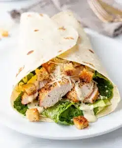 Sliced chicken Caesar wrap reveals tender chicken crisp lettuce and creamy dressing