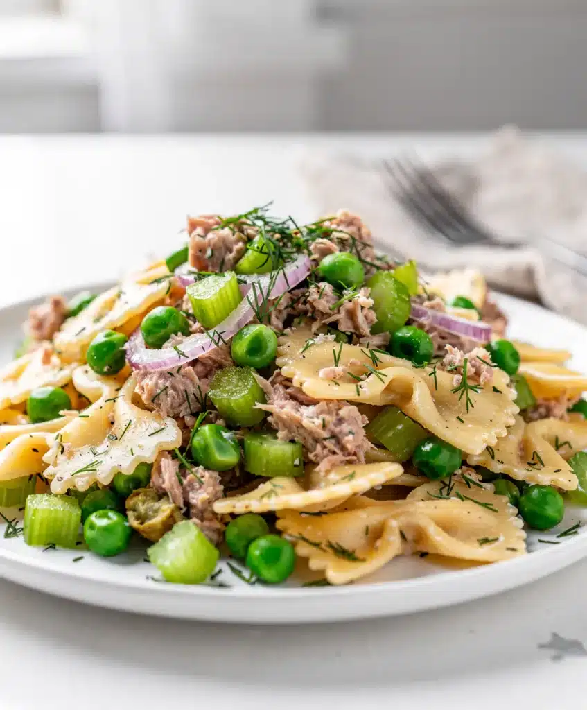 Creamy tuna pasta salad with bowtie pasta peas and celery in white bowl