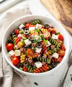 Colorful Italian pasta salad with rotini, salami, and fresh vegetables in a bowl.