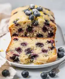 Moist lemon blueberry loaf cake with glaze on rustic wooden cutting board
