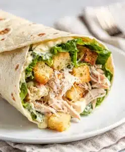 Make ahead chicken Caesar wrap sliced open on a rustic wooden board.