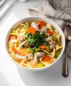 Make ahead cozy chicken noodle soup in a rustic white bowl with vegetables