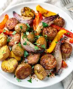 Crispy sausage and tender roasted vegetables on a white sheet pan
