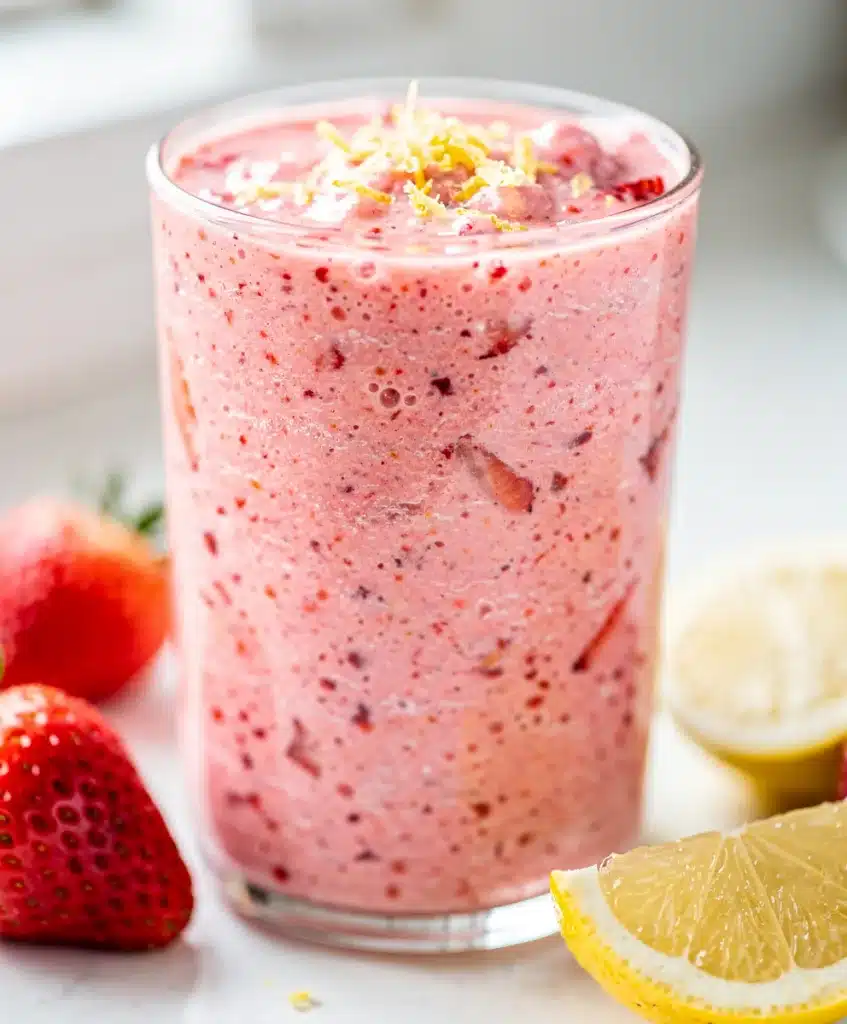 Refreshing strawberry lemonade smoothie in a tall glass with fruit garnish.