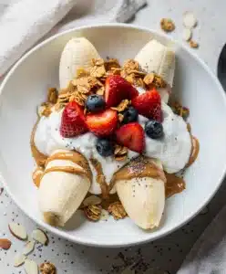 Healthy breakfast banana split bowl with yogurt, fresh berries, and crunchy granola.