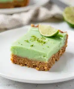 Creamy key lime pie bars with whipped cream on a rustic wood background.
