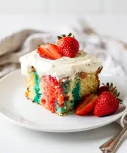 Colorful strawberry jello poke cake slice with fluffy frosting and fresh berries