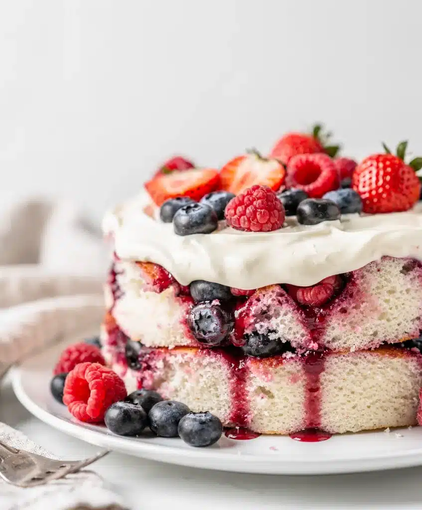 Summer berry poke cake with juicy holes and fluffy whipped cream topping