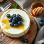 Close-up of a creamy cheesecake with a smooth cream cheese filling, topped with fresh blueberries and honey drizzle.