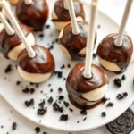 A close-up view of cookies and cream cake pops on a decorative tray, dipped in chocolate, with crushed Oreos sprinkled around