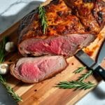 Perfectly roasted prime rib with golden crust, sliced to reveal tender, pink interior on a wooden cutting board with rosemary and garlic.