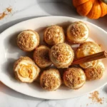 No-bake pumpkin cheesecake balls on a white platter, coated in graham crackers and garnished with cinnamon sticks.