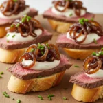 Steak crostini with horseradish sauce and caramelized onions on rustic board.