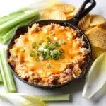 Creamy Buffalo chicken dip in a skillet with tortilla chips and celery.