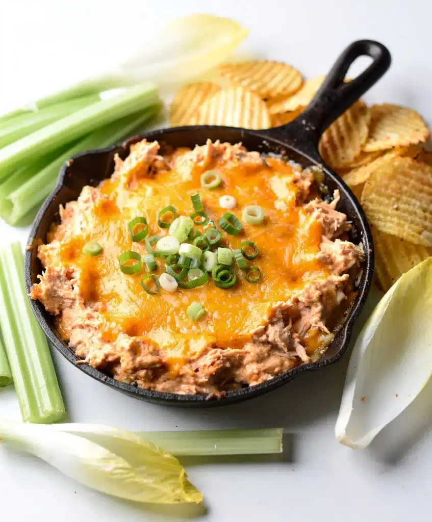 Creamy Buffalo chicken dip in a skillet with tortilla chips and celery.
