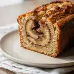 Moist cinnamon swirl banana bread slice with golden crumb and banana garnish.