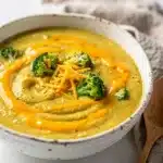 Creamy broccoli cheddar soup in a white bowl on rustic wooden table.