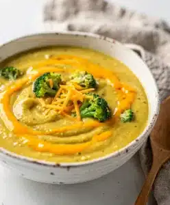 Creamy broccoli cheddar soup in a white bowl on rustic wooden table.