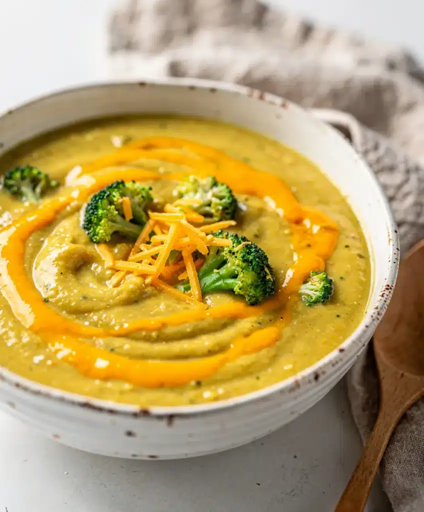 Creamy broccoli cheddar soup in a white bowl on rustic wooden table.