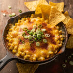 Creamy hot corn dip with melted cheese in a rustic cast iron skillet.