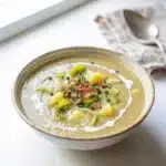 Creamy potato leek soup in a rustic bowl with chives and bread.