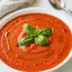 Creamy tomato basil soup recipe in a rustic bowl with fresh basil garnish