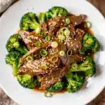 Crockpot beef and broccoli with rice in a white bowl on wood.