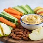 Healthy snack platter with fresh vegetables hummus almonds and apple slices