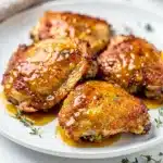 Crispy honey mustard chicken thighs with glossy sauce on a white plate.