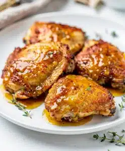 Crispy honey mustard chicken thighs with glossy sauce on a white plate.