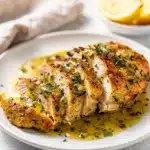 Slow cooker lemon herb chicken with creamy sauce and fresh herbs plated.