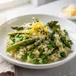 Vibrant spring vegetable risotto with asparagus and peas on white plate.