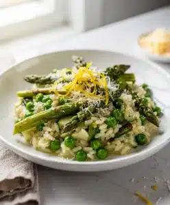 Vibrant spring vegetable risotto with asparagus and peas on white plate.