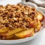 Warm apple cinnamon crisp with vanilla ice cream and caramel sauce in a bowl.