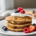 Fluffy banana oatmeal pancakes topped with honey and fresh fruit on rustic table