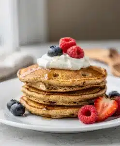 Fluffy banana oatmeal pancakes topped with honey and fresh fruit on rustic table