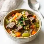Hearty beef barley soup with tender beef, vegetables, and pearl barley in a rustic bowl.