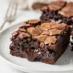 Classic fudgy brownies with crackly top on a white plate close up