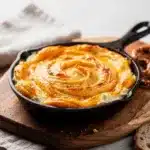 Creamy baked Irish Pub Cheese Dip in a ramekin with soft pretzel bites.