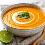 Creamy ginger carrot soup garnished with cilantro and lime in a bowl.