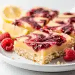 Lemon raspberry bars with powdered sugar on a rustic wooden table.