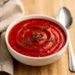 Creamy roasted red pepper soup in a rustic bowl with bread and basil